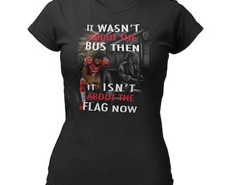 May include: Black t-shirt with a graphic of a football player on a bus. The text "It wasn't about the bus then. It isn't about the flag now." is printed on the shirt.