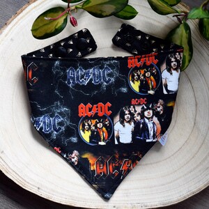 May include: Black bandana featuring a white and red AC/DC logo and band photos. The bandana has a black and white hand print pattern on the reverse.