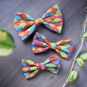 May include: Three colourful bow ties with a geometric pattern of overlapping circles in shades of green, blue, pink and yellow.