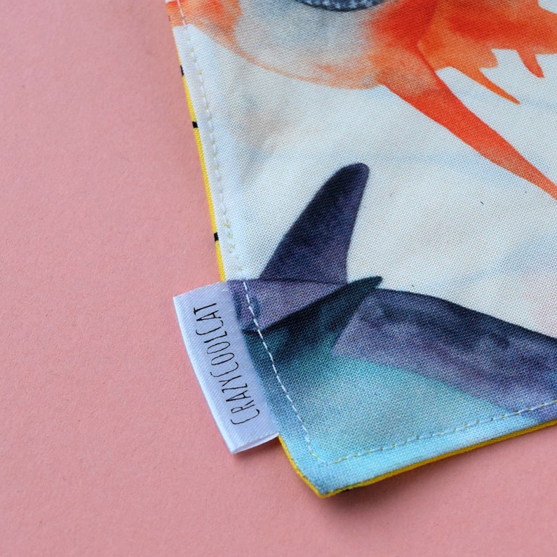 May include: A fabric item featuring a watercolour print of a dark blue origami-style bird against a light background with orange accents. A white fabric tag is sewn into the side seam, clearly displaying the black text CRAZYCOOLCAT in a sans-serif font.