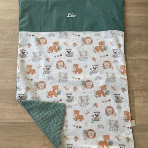 Peut inclure: Une couverture rectangulaire avec une section supérieure vert foncé unie portant le prénom Léo brodé en blanc. Le corps principal présente un fond blanc avec un motif répétitif de lions, d'éléphants et de lémuriens, avec un revers vert texturé.