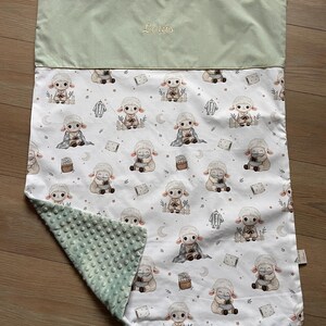 Può includere: Una coperta per bambini con una parte superiore verde chiaro e un fondo a fantasia bianca. Il motivo presenta pecore dei cartoni animati, lune e stelle. Il nome "Louis" è ricamato sulla parte superiore.