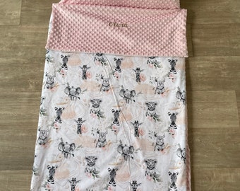 May include: A nap mat set featuring a light pink dimple-textured pillow and a matching top flap embroidered with the name Olivia. The main blanket displays a repeating pattern of illustrated baby safari animals, including zebras, elephants, and lions, accented with soft pink floral motifs on a white background.