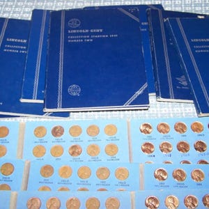 May include: A collection of Lincoln Head Cent albums and coin holders. The blue albums are labeled "Lincoln Cent Collection Starting 1941 Number Two." The coin holders are light blue and filled with copper pennies.
