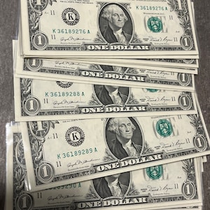 May include: A stack of five one dollar bills, all with the same serial number, K 36189276 A. The bills are in good condition and have a green seal.