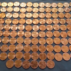 May include: A large collection of copper-colored US pennies arranged in a grid pattern. The pennies are all facing the same direction, with the heads of Abraham Lincoln visible on each coin.