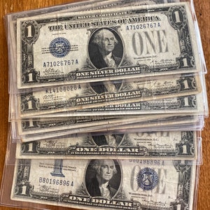 May include: A stack of ten vintage US one dollar silver certificates. The bills are in good condition and feature a portrait of George Washington. The serial numbers are visible on each bill.