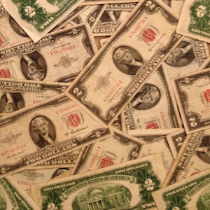 May include: A close-up of a pile of vintage two dollar bills. The bills are faded and worn, with some showing signs of wear and tear. The bills are all from the United States of America.
