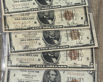 May include: Five $5 bills from different Federal Reserve Banks, including Boston, New York, Philadelphia, Kansas City, and a fourth bank with an unclear location. Each bill features a portrait of Abraham Lincoln and the text "FIVE DOLLARS".