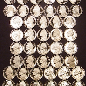 May include: A collection of silver-colored United States nickel coins, each displaying a profile of Thomas Jefferson and the words "Liberty" and "In God We Trust." The coins are arranged in neat rows and columns.