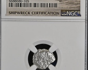 May include: A silver coin from the El Cazador shipwreck, certified by NGC. The coin is in a plastic slab with a white background and a black label that reads "(1772-83) MEXICO 1/2R EL CAZADOR GENUINE 6688680-165 SHIPWRECK CERTIFICATION NGC".