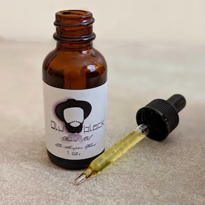 Puede incluir: Una botella de vidrio marrón con un gotero, etiquetada "Old Black Beard Oil The Hampton Blend 1 oz.", con una ilustración de dibujos animados de un hombre con barba y un sombrero.