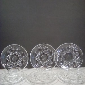 May include: Set of six clear glass dessert plates with a starburst pattern. The plates are stacked in two rows of three.