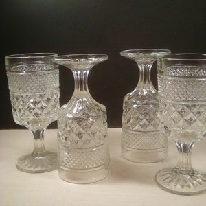 May include: Four clear, vintage-style goblets with diamond-patterned detailing. Two are upright, and two are inverted, showcasing the stem and base. The glasses are made of clear glass and sit on a white surface against a black background.