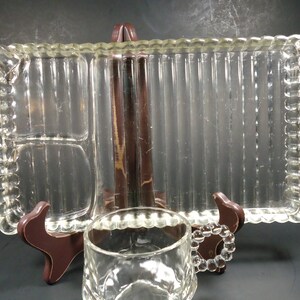 May include: A clear glass serving tray with a beaded edge and divided compartments. The tray is on a brown wooden stand.