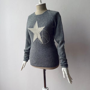 May include: A gray knitted sweater with a white star and peace sign design.