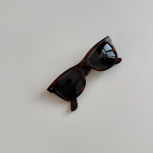 May include: Classic tortoiseshell sunglasses with dark lenses. The frames have a rectangular shape and a glossy finish. The sunglasses are angled slightly, showcasing the design and style. A timeless accessory for eye protection.