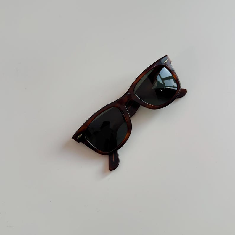 May include: Classic tortoiseshell sunglasses with dark lenses. The frames have a rectangular shape and a glossy finish. The sunglasses are angled slightly, showcasing the design and style. A timeless accessory for eye protection.