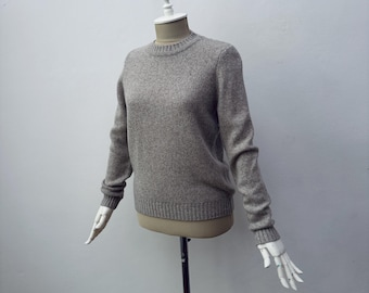 May include: A light gray crew neck sweater displayed on a mannequin. The sweater has long sleeves and ribbed cuffs and hem. The fabric appears soft and textured. The mannequin has a white head and hands.