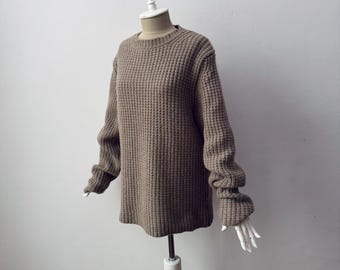 May include: A brown, waffle-knit sweater displayed on a mannequin. The sweater has a crew neck and long sleeves. The fabric has a textured appearance. The mannequin is white and has a neutral background.