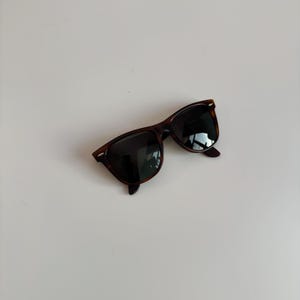 May include: Sunglasses with a classic design. The frames are a dark brown tortoiseshell pattern, and the lenses are black. The sunglasses are angled slightly, showing the shape of the frames and lenses.