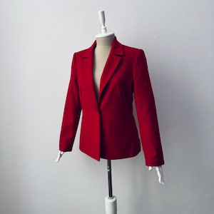 May include: A vibrant red blazer displayed on a mannequin. The blazer features a classic notched lapel, long sleeves, and a single-button closure. The tailored fit and rich color suggest a professional or formal style.