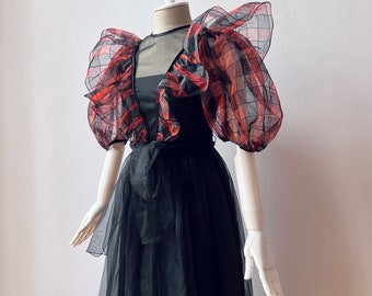 May include: A black dress with a red and black checked overlay. The dress has puffed sleeves and a full skirt.