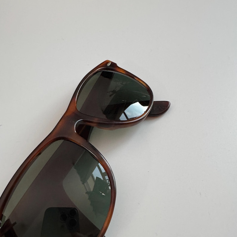 May include: Tortoiseshell sunglasses with dark lenses. The frames have a classic, angular shape. The sunglasses are set against a white background.