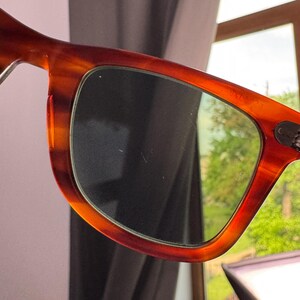 May include: Close-up of sunglasses with a tortoiseshell pattern frame. The lenses are dark, and the frame has a warm, reddish-brown hue. The design is classic and stylish, suitable for everyday wear.