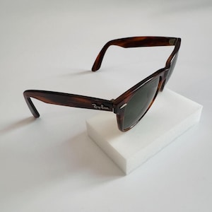 May include: Brown tortoiseshell sunglasses with dark lenses. The Ray-Ban logo is visible on the temple. The sunglasses are set against a white background.