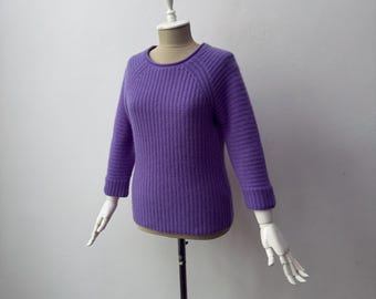 May include: A vivid purple sweater with a ribbed knit design. The sweater features a crew neck and three-quarter length sleeves. The garment is displayed on a mannequin with articulated white hands.