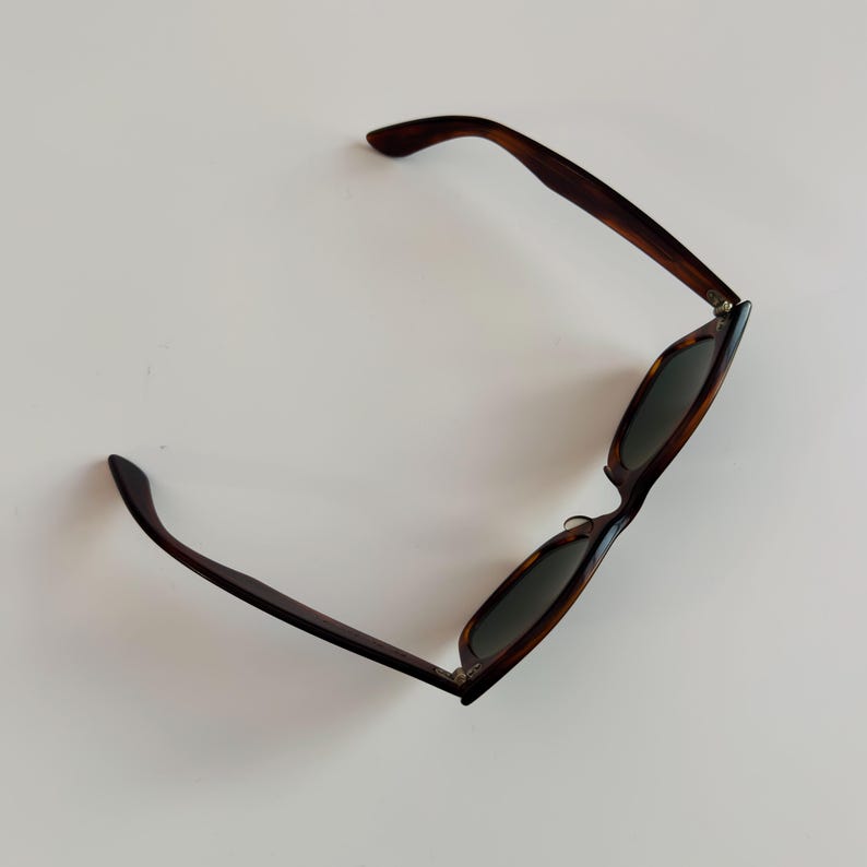May include: Sunglasses with a tortoiseshell pattern frame and dark lenses. The arms of the sunglasses are a dark brown color. The sunglasses are angled, showing the shape of the lenses and the frame.
