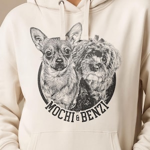May include: A cream-colored hooded sweatshirt featuring a black and white circular graphic on the chest. The graphic depicts two dogs with the text MOCHI & BENZI printed in a bold, sans-serif font along the bottom edge of the circular design.