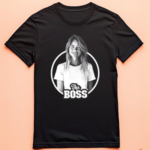 May include: Black t-shirt with a white circle graphic featuring a woman's portrait and the text "The Boss".