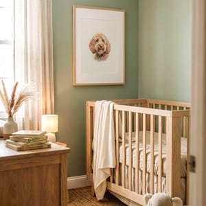 May include: A light wood crib with vertical slats, draped with a cream-colored textured blanket. Above the crib hangs a framed portrait of a golden-brown dog. A plush gray elephant toy sits on the floor near the crib in a room with sage green walls.