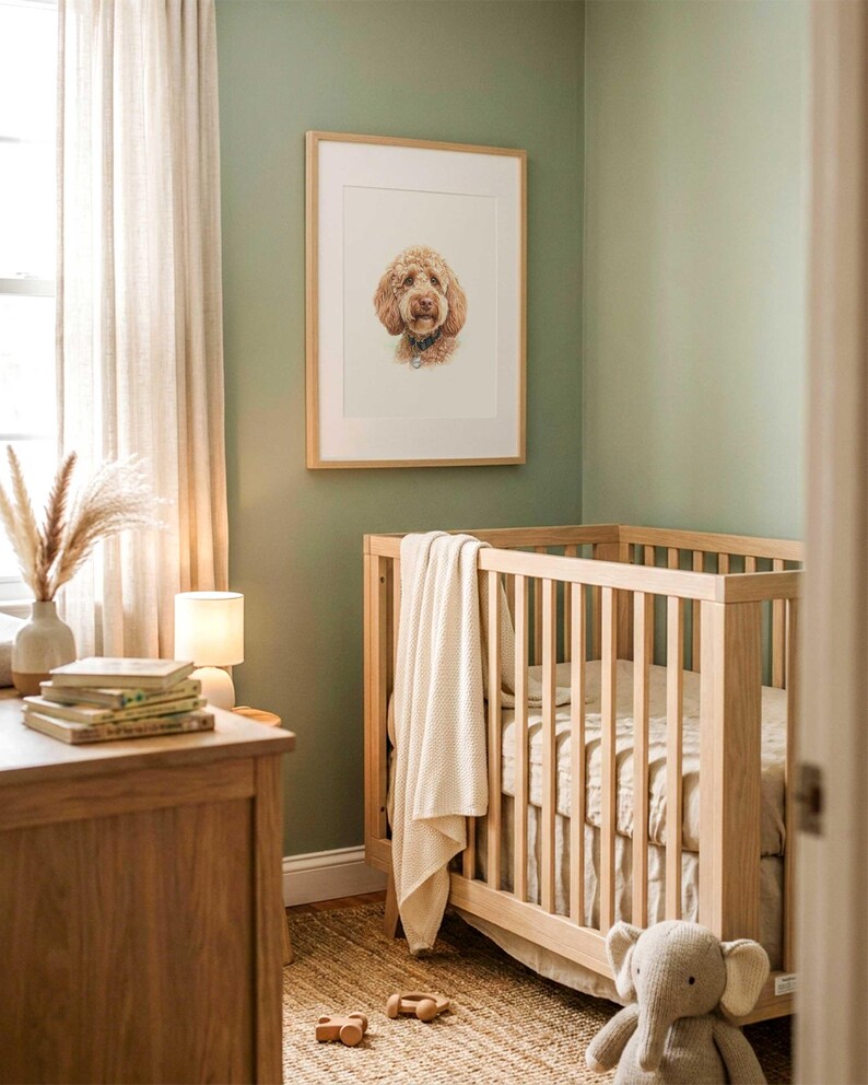 May include: A light wood crib with vertical slats, draped with a cream-colored textured blanket. Above the crib hangs a framed portrait of a golden-brown dog. A plush gray elephant toy sits on the floor near the crib in a room with sage green walls.