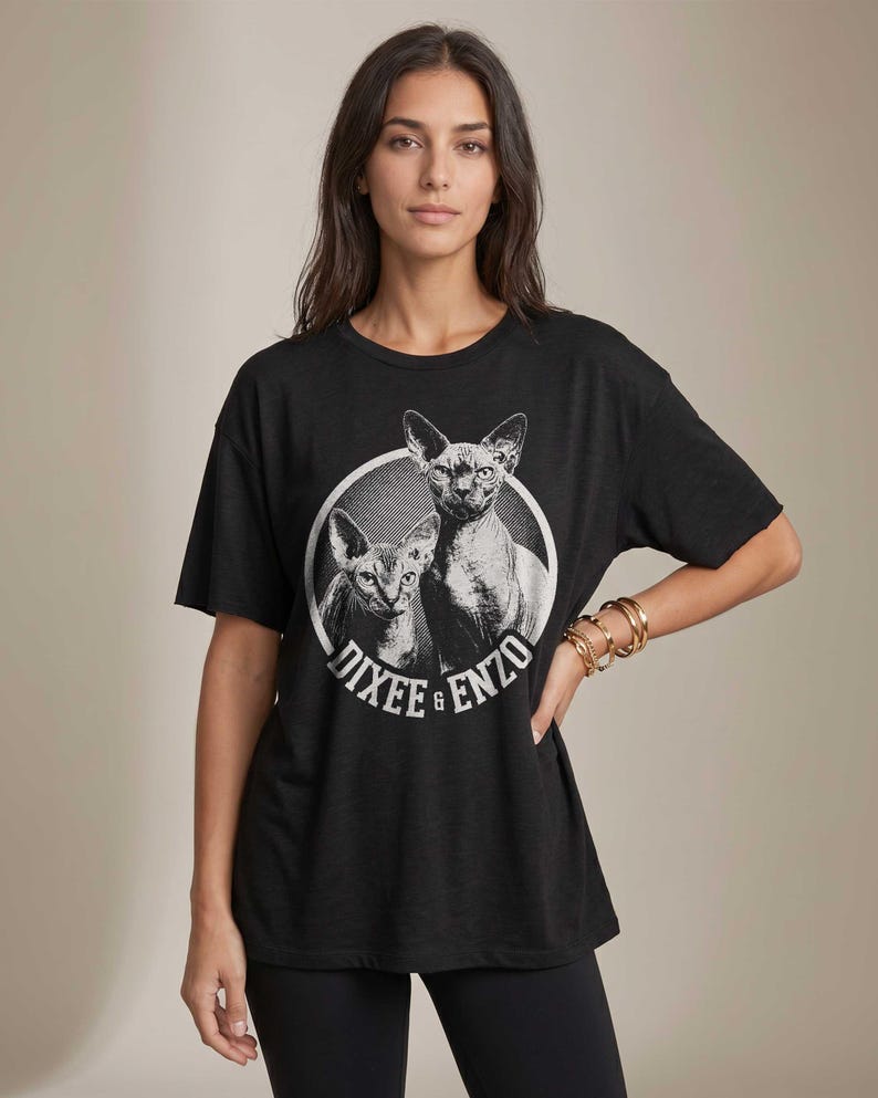 Puede incluir: Camiseta negra con un gr&aacute;fico de dos gatos Sphynx dentro de un c&iacute;rculo blanco. El texto "Dixee & Enzo" est&aacute; impreso alrededor del c&iacute;rculo. La camiseta tiene mangas cortas y un corte holgado.