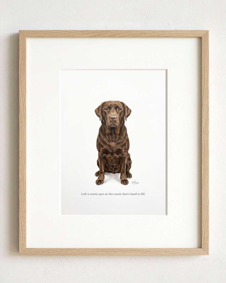 A pastel portrait of a chocolate-brown dog in a light oak frame with a wide white mount, photographed straight on against a plain pale wall.