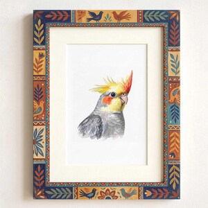 May include: A framed watercolor painting of a cockatiel with a yellow crest, orange cheek patches, and gray feathers. The frame features a decorative border with repeating patterns of blue, orange, and yellow birds, leaves, and geometric shapes.