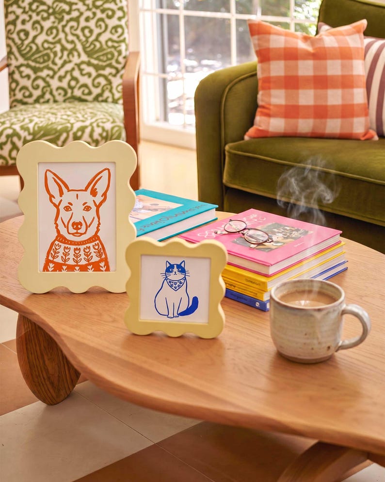 Op de afbeelding: Twee lichtgele fotolijsten met een geschulpte rand. De grotere rechthoekige lijst bevat een oranje illustratie van een hond in een trui met patroon. De kleinere vierkante lijst bevat een blauwe illustratie van een kat met een bandana.