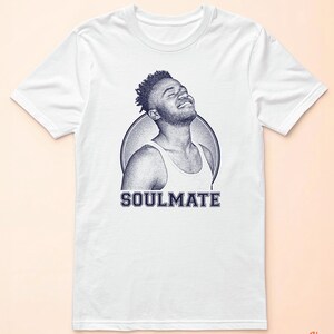 May include: White t-shirt featuring a blue and white illustration of a person with the word "SOULMATE" printed below.