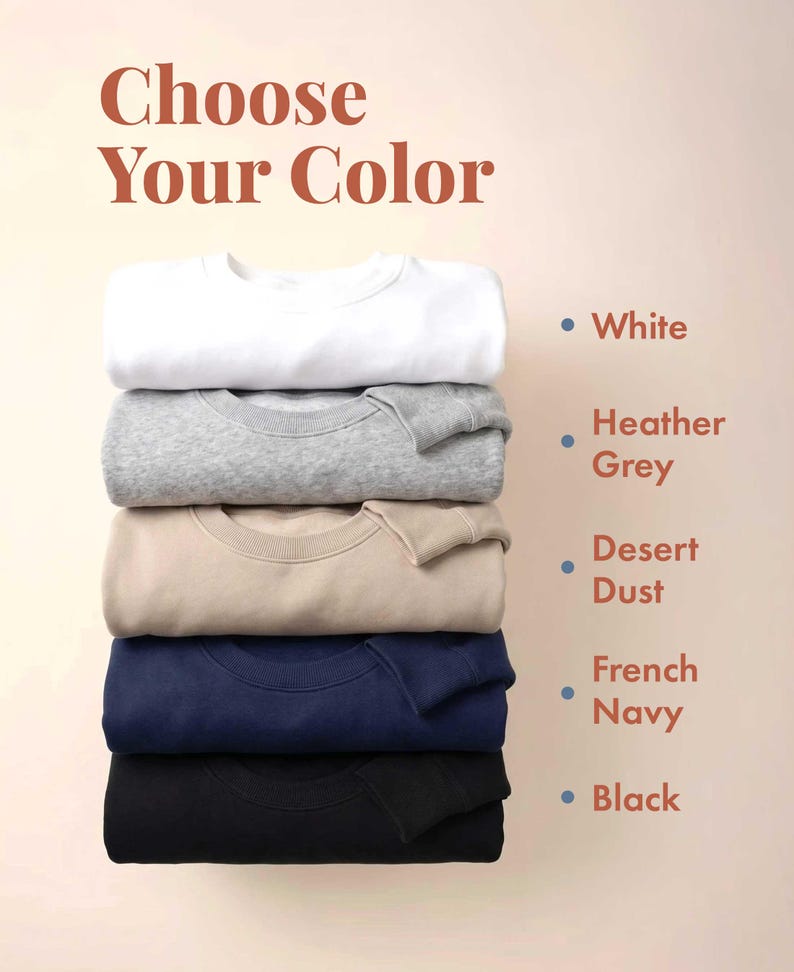 May include: A stack of five crewneck sweatshirts in white, heather grey, desert dust, french navy, and black. The text "Choose Your Color" appears at the top, with color names listed next to corresponding dots matching each sweatshirt color.