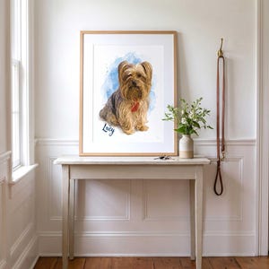May include: A framed portrait print featuring a watercolor illustration of a Yorkshire Terrier dog with long tan and brown fur. The dog is set against a blue watercolor splash background with the name Lucy written in cursive script below the dog.