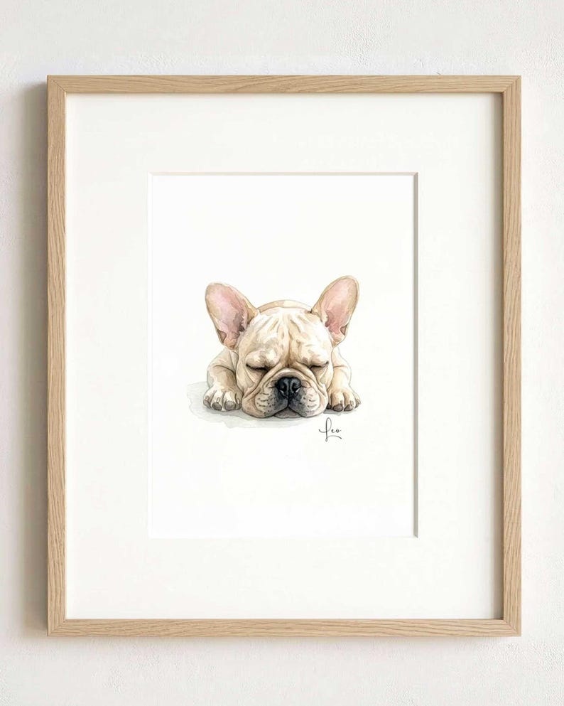 A framed watercolor illustration of a sleeping cream-colored French Bulldog with large ears and a black nose. The artwork is centered within a light-toned wooden frame, featuring a signature in the bottom right corner of the painting.