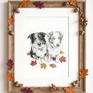 May include: A framed charcoal-style drawing of two dogs sitting together, surrounded by colorful autumn leaves. The wooden frame is decorated with small acorns and oak leaves in shades of orange, red, and brown, creating a seasonal display.