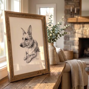 以下が含まれることがあります： 尖った耳と首輪をした犬の木炭画が額装されており、右下に筆記体でBenjiという名前が書かれています。このアートワークは、白いマット枠が付いた素朴な中間色の木製フレームに収められています。