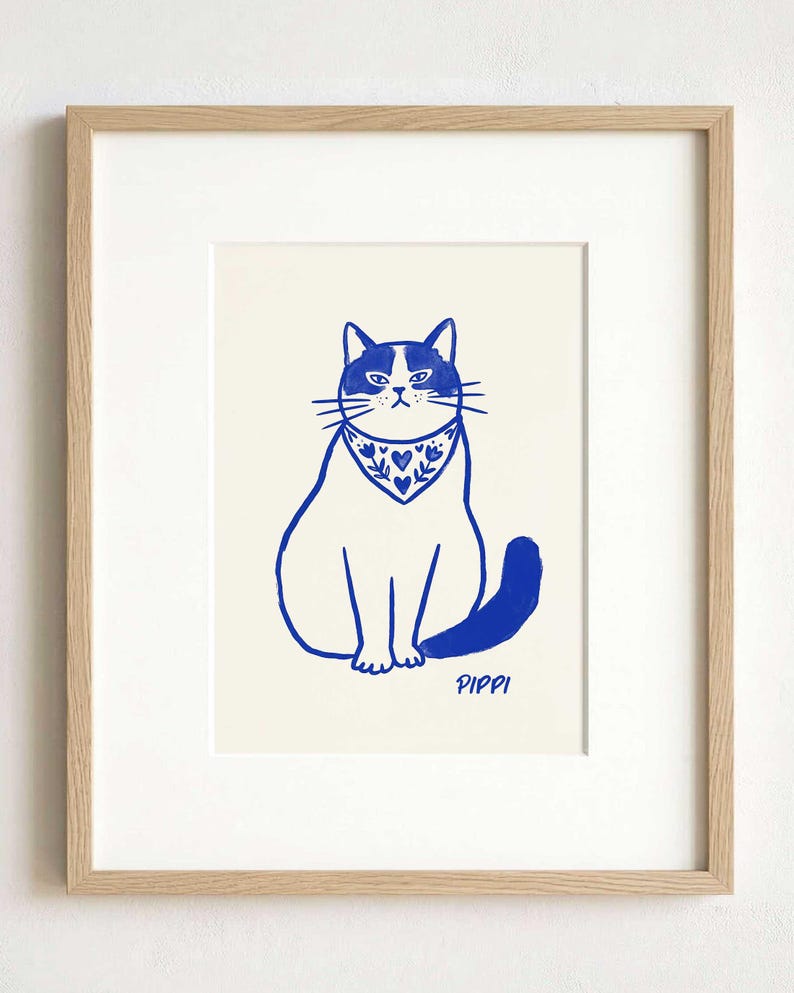 A framed art print featuring a blue ink illustration of a cat wearing a patterned bandana with hearts and floral motifs. The cat is sitting upright, and the name PIPPI is printed in blue ink below the cat on a cream background.