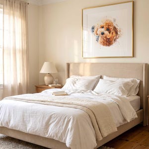 May include: A square framed wall art piece featuring a watercolor-style portrait of a brown curly-haired dog. The artwork is displayed in a thin gold frame with a white mat, hanging on a light beige wall above a neutral-toned upholstered bed.