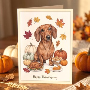 A greeting card featuring a brown dachshund sitting in the center, surrounded by autumn leaves, pumpkins, a roasted turkey on a platter, a basket of rolls, and a slice of pumpkin pie, with the text Happy Thanksgiving at the bottom.