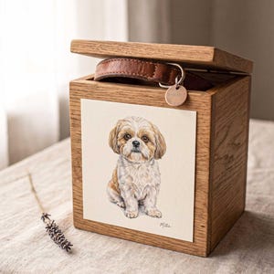 A pastel dog portrait mounted on the lid of a small wooden keepsake box with a brass clasp, standing on a neutral surface against a warm plain background.